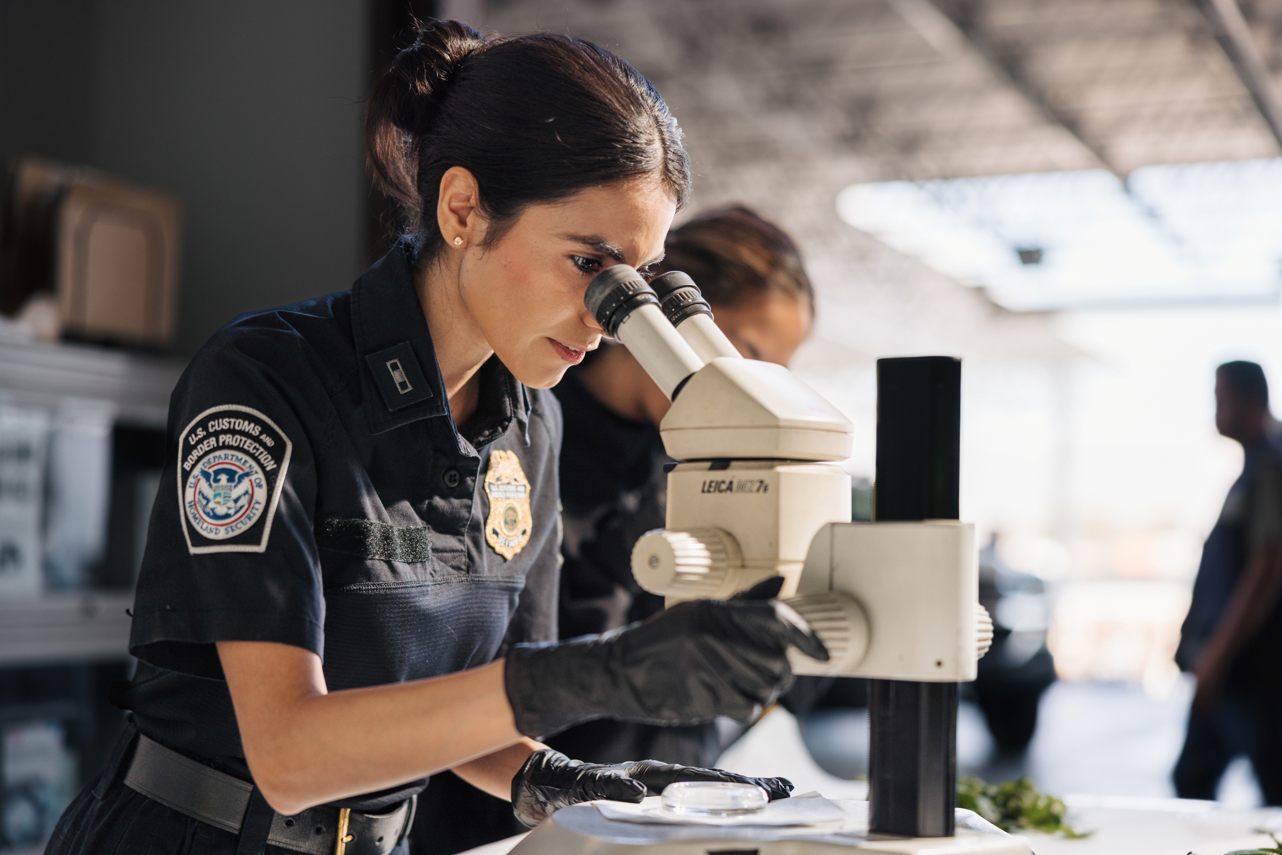 Female CBP officer in uniform working in a lab with a microscope.